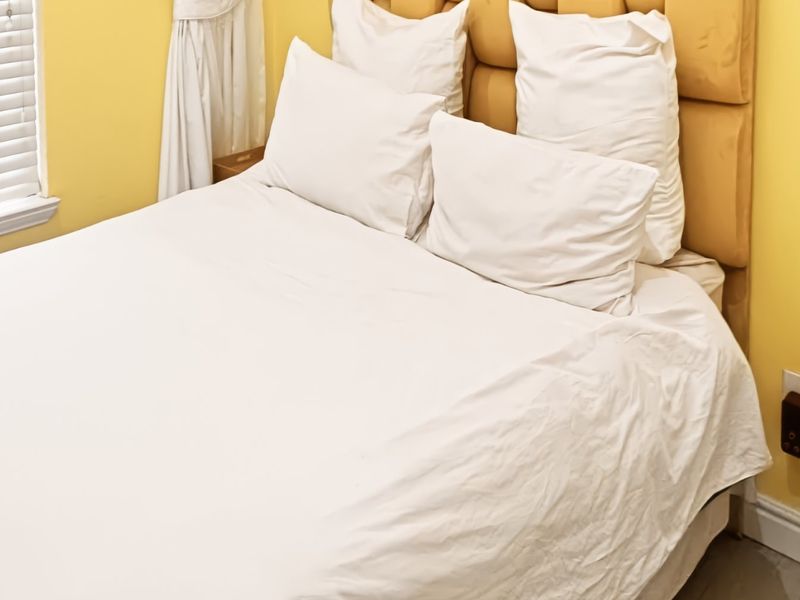 A cozy bedroom featuring yellow walls, white venetian blinds, and neutral flooring, providing a bright and functional sleeping space.