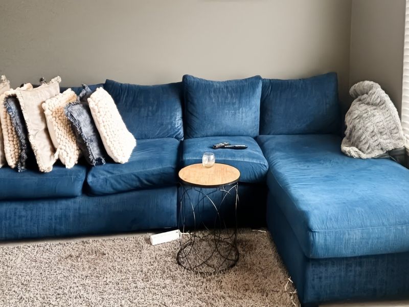 A comfortable living room area featuring neutral wall tones and large windows fitted with venetian blinds, providing natural light to the space.