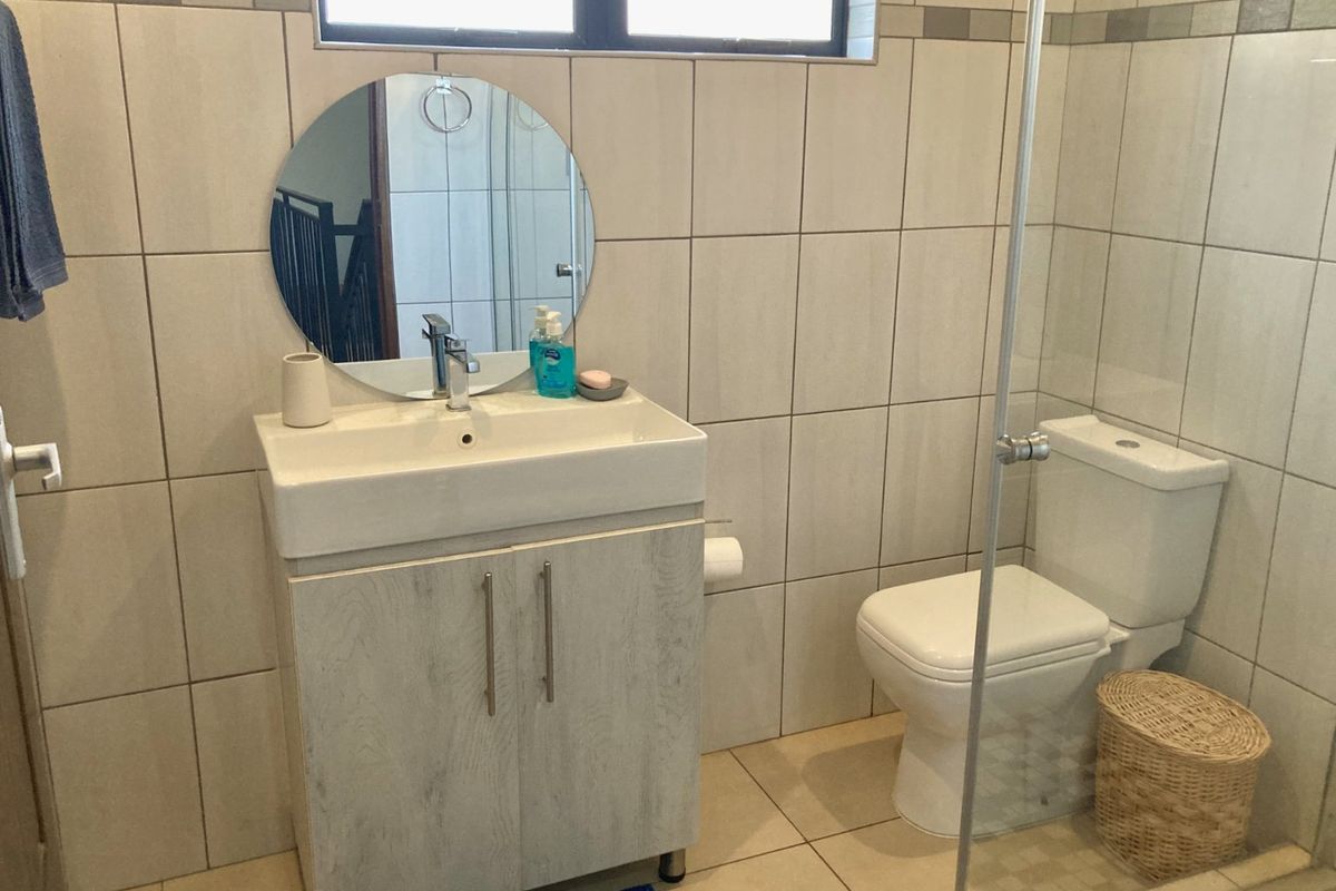 A functional bathroom featuring a modern vanity cabinet, ceramic basin, toilet, and a glass-enclosed shower with neutral wall and floor tiling.