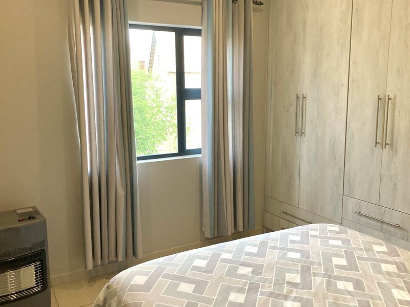 A well-maintained bedroom featuring built-in cupboards, tiled flooring, and an aluminium window frame, offering a clean and functional living space.