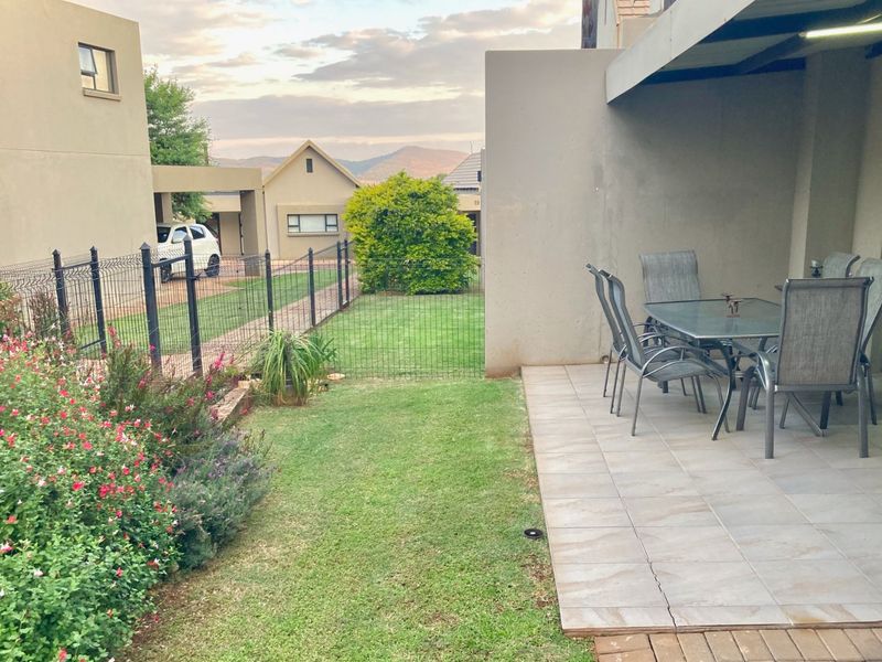 A covered patio area with tiled flooring overlooking a private garden and fenced yard, featuring mountain views in the background.