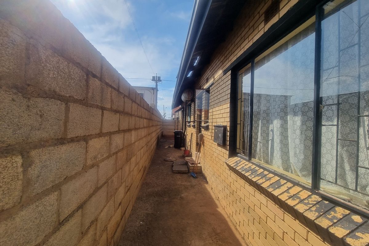 Side passage of the property featuring a brick boundary wall, brick exterior facade, and windows with security bars.
