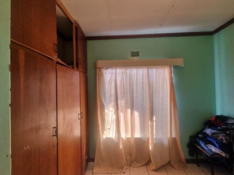 A bedroom featuring built-in wooden cupboards and tiled flooring, requiring cosmetic updates to improve the overall aesthetic and condition.