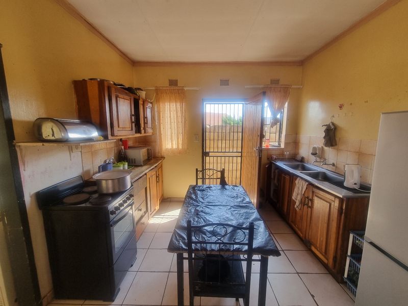A functional kitchen featuring wooden cabinetry, double basin sink, and tiled flooring, with direct access to the rear exterior through a security gate.