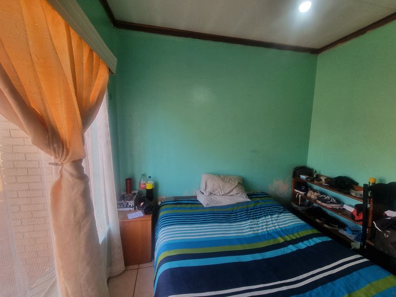 A bedroom featuring tiled flooring and a window, currently showing signs of wear on the walls requiring maintenance or repainting.