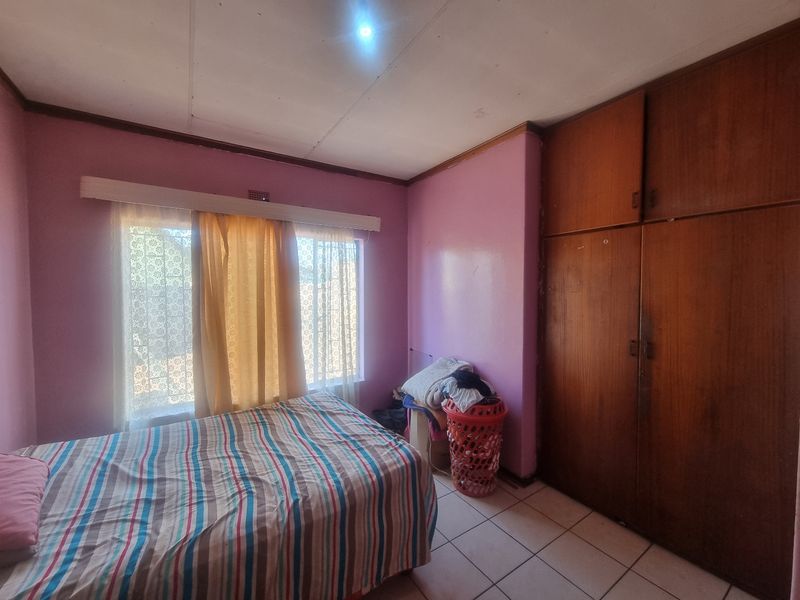 A bedroom featuring built-in wooden wardrobes, tiled flooring, and security bars on the window. The room requires cosmetic updates to improve its overall condition.