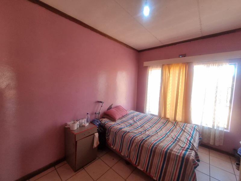 A bedroom featuring tiled flooring and large windows with curtain rails, requiring cosmetic updates to the walls and ceiling.