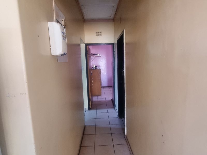 A functional hallway featuring tiled flooring, a ceiling access hatch, and a wall-mounted electrical distribution board, connecting to adjacent rooms.