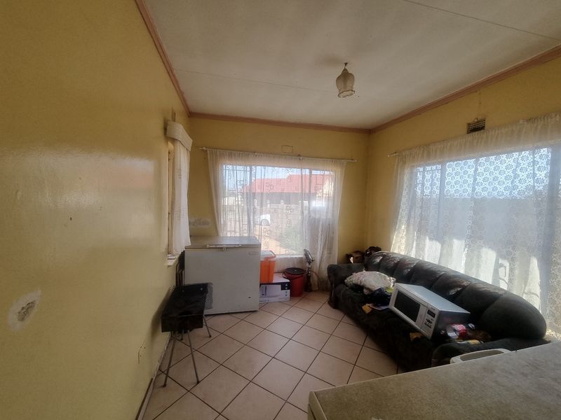 A living area featuring tiled flooring and natural light through large windows with security bars, requiring cosmetic updates to the walls and ceiling.