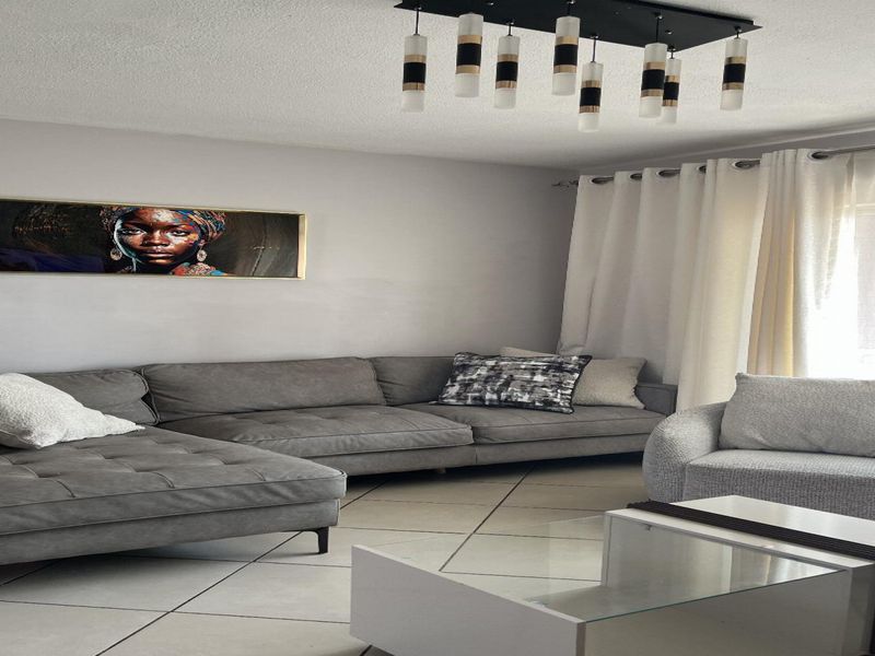 A well-lit living room featuring neutral tiled flooring, a contemporary multi-pendant light fixture, and access to an outdoor area through a sliding glass door.