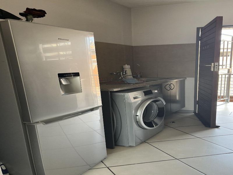 A functional laundry area featuring tiled flooring, a stainless steel sink with splashback, and direct access to an outdoor space.