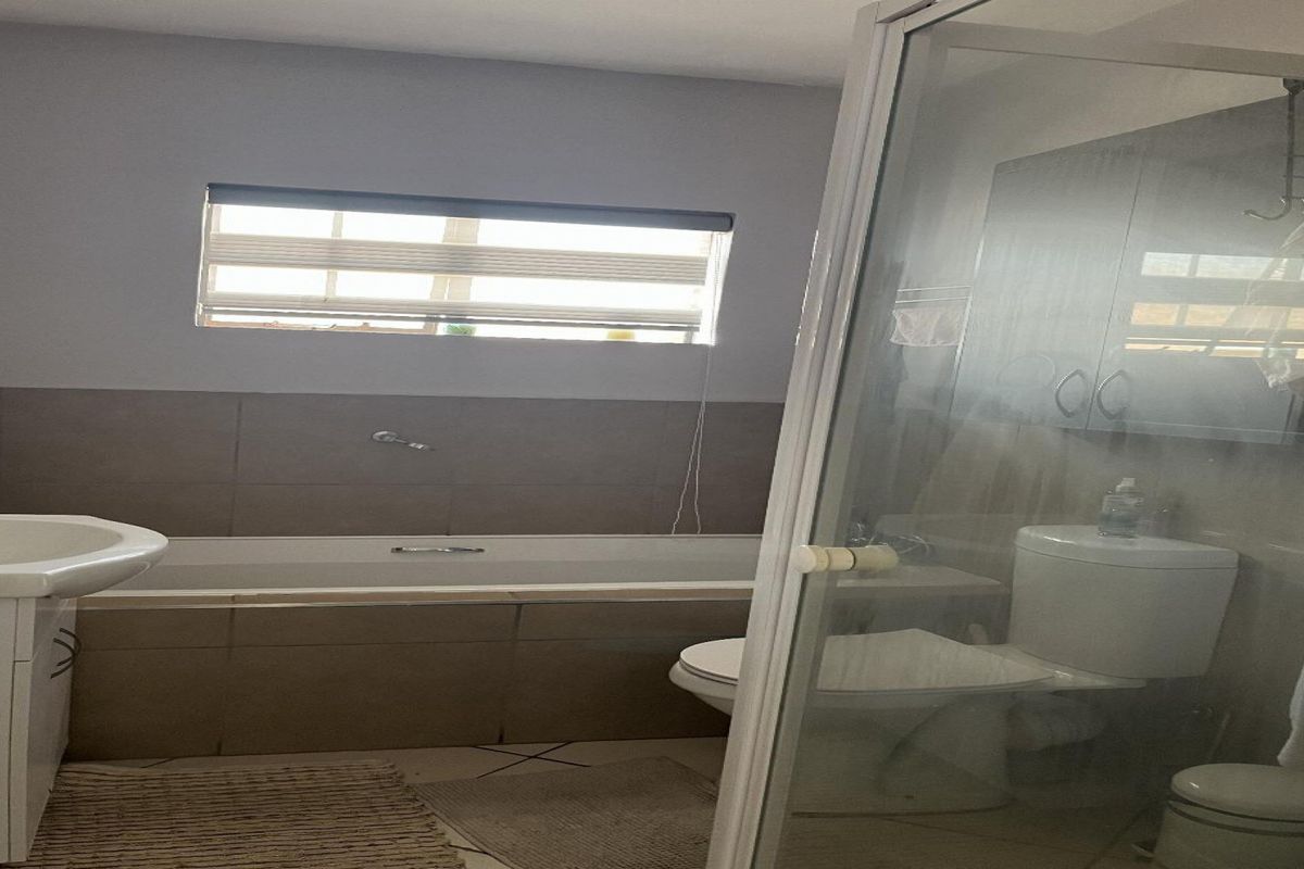 A functional bathroom featuring a built-in bathtub, separate shower enclosure, toilet, and vanity basin with tiled finishes.