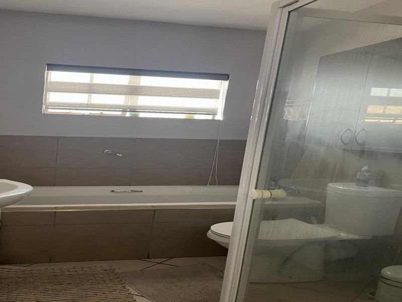 A functional bathroom featuring a built-in bathtub, separate shower enclosure, toilet, and vanity basin with tiled finishes.