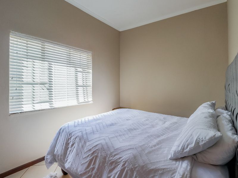 A neutrally painted bedroom featuring tiled flooring, coved ceilings, and fitted venetian blinds, offering a clean and functional living space.