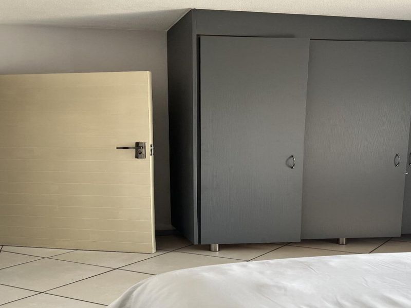 A bedroom featuring tiled flooring and a large, modern dark grey built-in wardrobe.