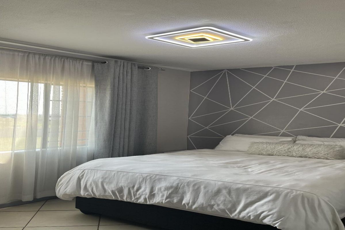 A well-maintained bedroom featuring tiled flooring, a modern square LED ceiling light, and a decorative geometric accent wall.