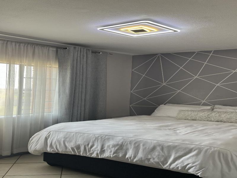 A well-maintained bedroom featuring tiled flooring, a modern square LED ceiling light, and a decorative geometric accent wall.