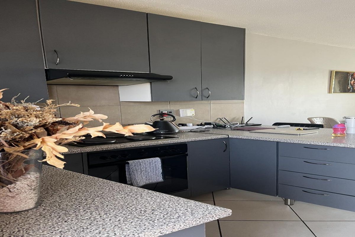 A modern kitchen featuring dark grey cabinetry, speckled laminate countertops, built-in oven, electric hob, and a tiled backsplash.