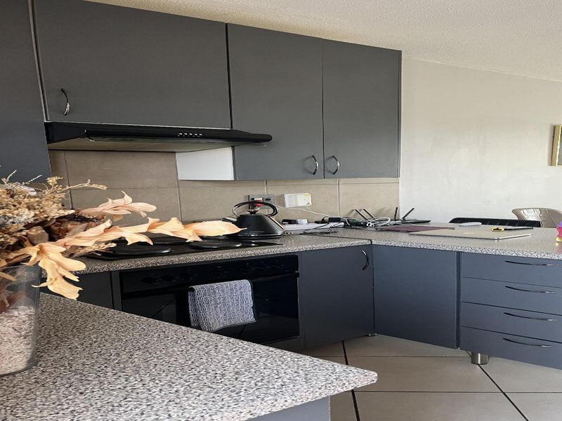 A modern kitchen featuring dark grey cabinetry, speckled laminate countertops, built-in oven, electric hob, and a tiled backsplash.