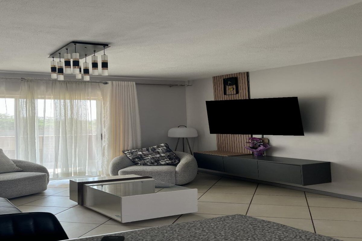 A bright and spacious living room featuring tiled flooring, a decorative feature wall, and a large sliding glass door leading to an outdoor area.