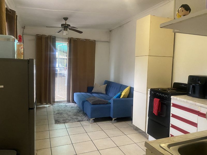 Open-plan living and kitchen area featuring tiled flooring, a ceiling fan, and built-in cabinetry, with direct access to an outdoor patio area.