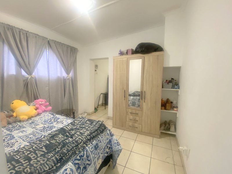 A bedroom featuring tiled flooring and built-in shelving, offering a functional space with neutral wall finishes.
