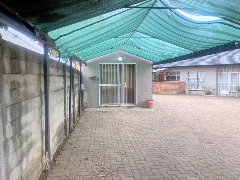 Rear exterior area featuring a paved driveway, a security-gated entrance, and a shade cloth canopy structure.