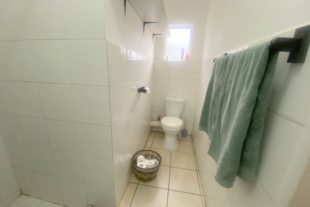 A compact bathroom featuring white wall tiles, tiled flooring, a standard toilet, and a wall-mounted towel rail.