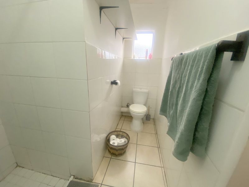 A compact bathroom featuring white wall tiles, tiled flooring, a standard toilet, and a wall-mounted towel rail.