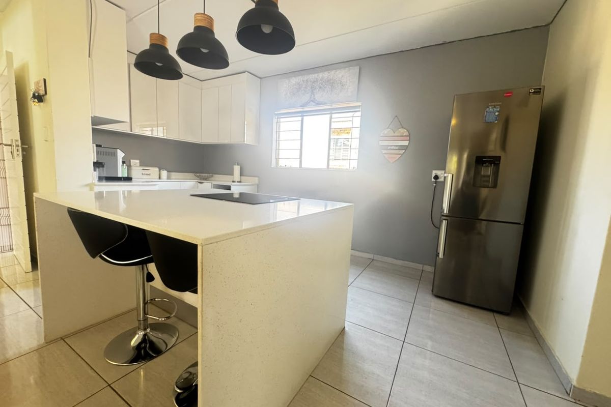 Modern kitchen featuring a central island with a built-in hob, white cabinetry, quartz countertops, and tiled flooring, offering a clean and functional workspace.
