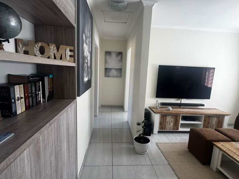 A well-maintained living area featuring modern tiled flooring, a built-in wooden shelving unit, and a neutral color palette throughout the space.