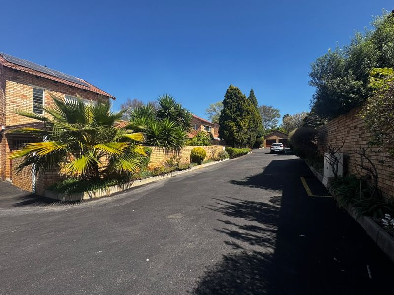 A view of the complex driveway featuring brick boundary walls, mature landscaping, and access to residential units with tiled roofs.