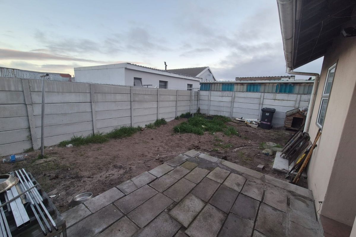 Rear exterior view featuring a paved patio area and a large, unlandscaped garden enclosed by precast concrete boundary walls.