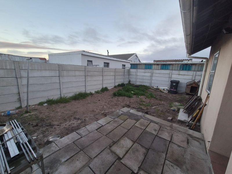 Rear exterior view featuring a paved patio area and a large, unlandscaped garden enclosed by precast concrete boundary walls.