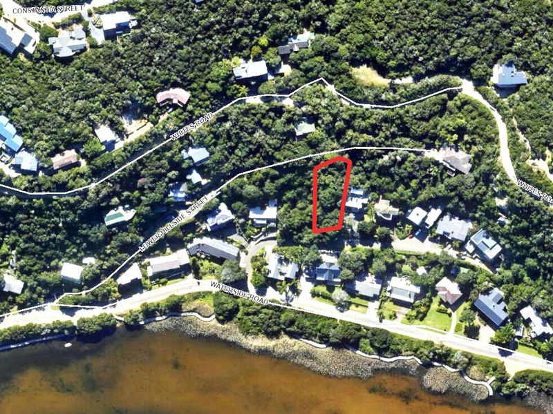 An aerial view showing a vacant residential land plot outlined in red, situated within a wooded neighborhood near the waterfront.