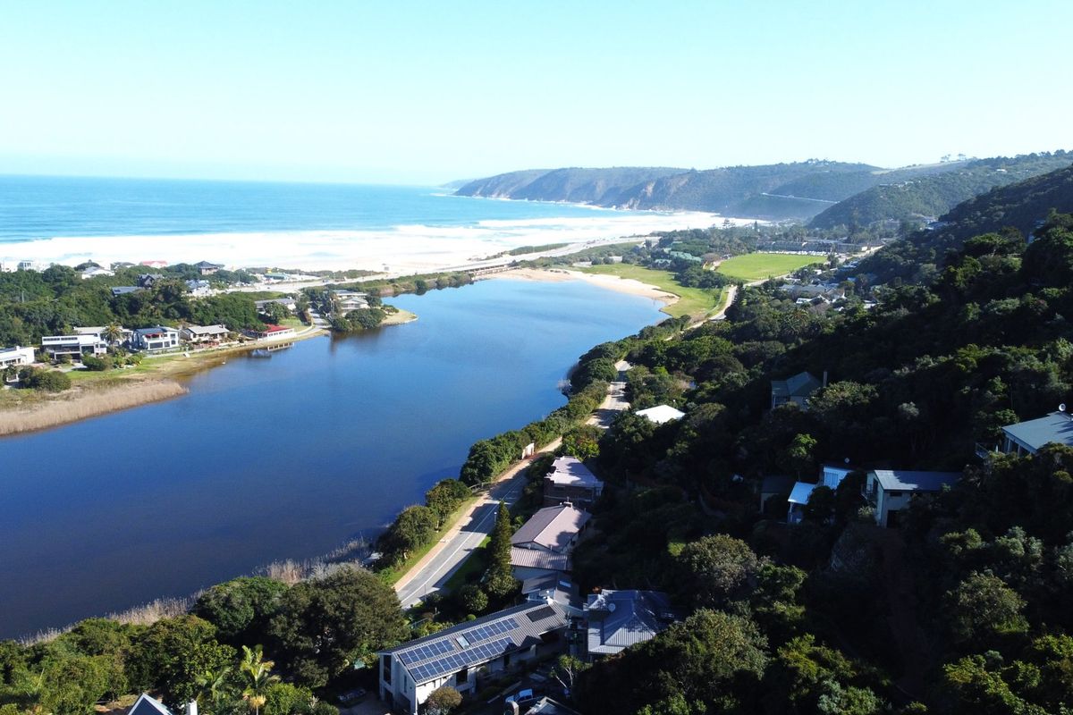 An aerial view of the coastal landscape, featuring an estuary, surrounding vegetation, and nearby residential properties.