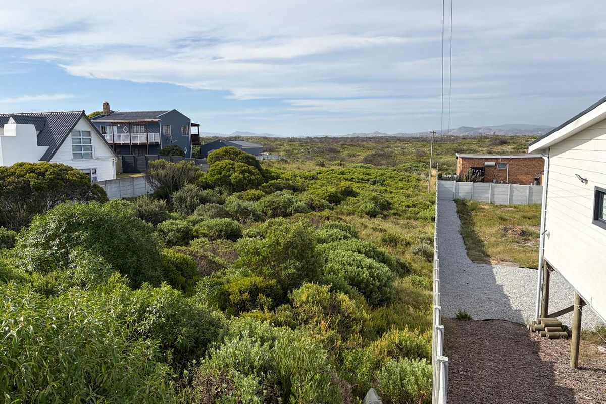 Elevated view overlooking a vacant residential plot with native coastal vegetation, gravel pathways, and surrounding residential properties.