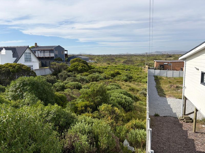 Elevated view overlooking a vacant residential plot with native coastal vegetation, gravel pathways, and surrounding residential properties.