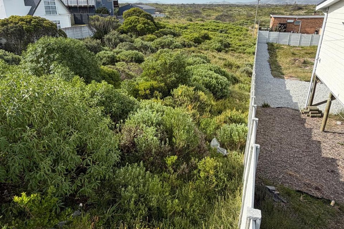 A view of the rear yard area featuring a precast concrete boundary wall, gravel ground cover, and natural coastal vegetation.