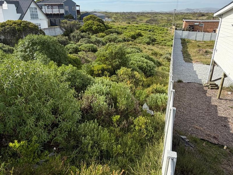 A view of the rear yard area featuring a precast concrete boundary wall, gravel ground cover, and natural coastal vegetation.
