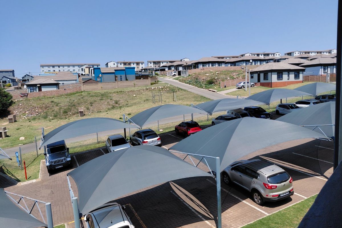 An elevated view of a residential complex parking area featuring multiple shade sail structures over paved parking bays.