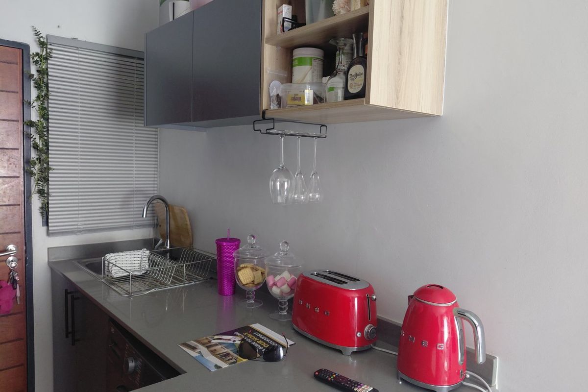 A compact kitchen area featuring modern grey and wood-tone cabinetry, a stone countertop, and a stainless steel sink with a mixer tap.