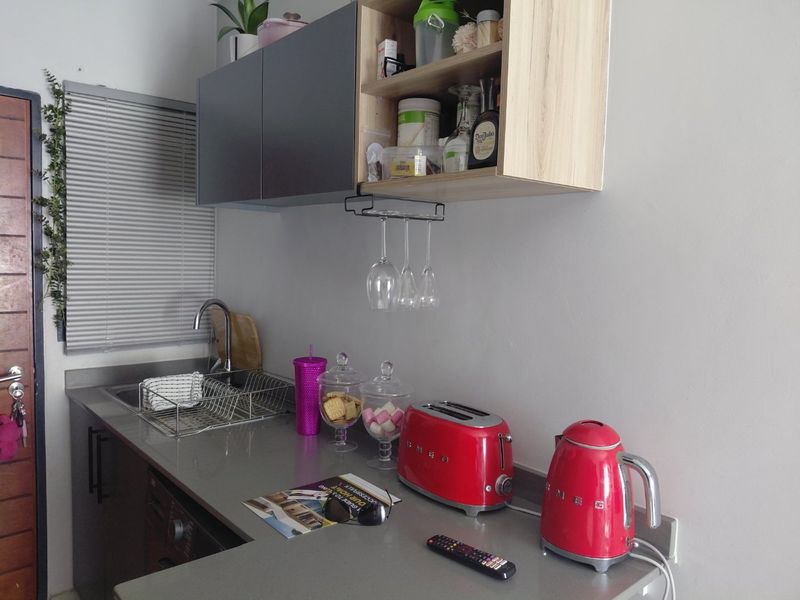 A compact kitchen area featuring modern grey and wood-tone cabinetry, a stone countertop, and a stainless steel sink with a mixer tap.