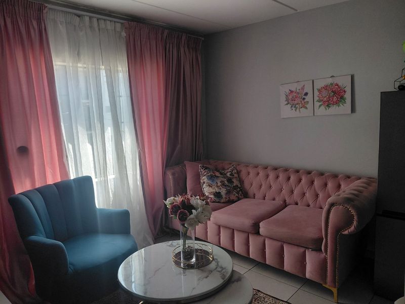 A cozy living room area featuring tiled flooring and large windows dressed with floor-to-ceiling curtains, providing a comfortable and well-lit space.