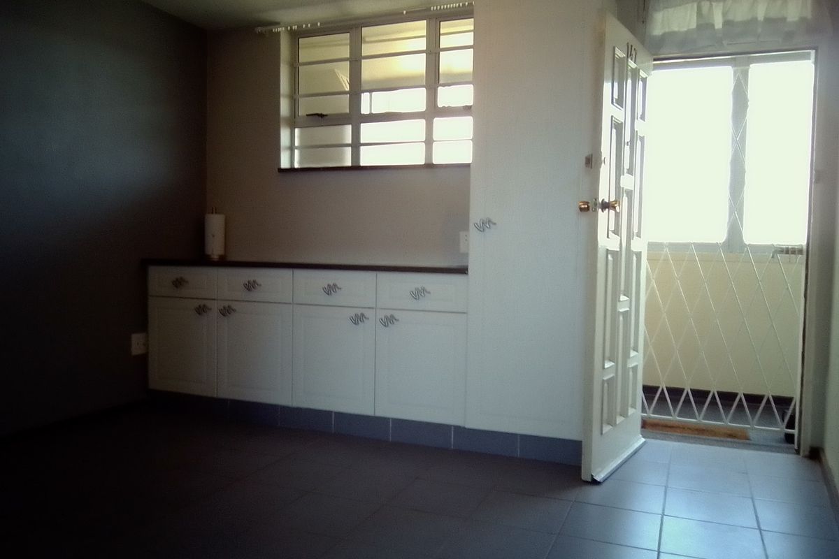 A functional kitchen area featuring built-in cabinetry, tiled flooring, and direct access to an exterior balcony through a secure door.