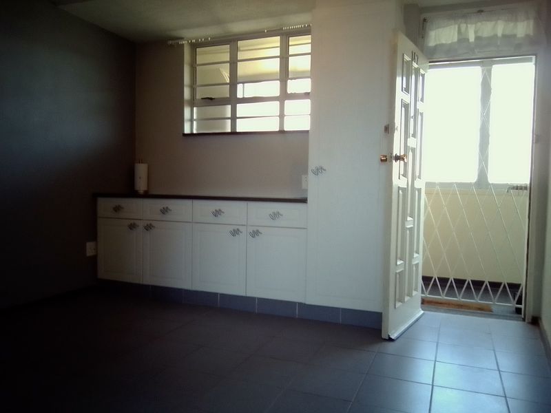 A functional kitchen area featuring built-in cabinetry, tiled flooring, and direct access to an exterior balcony through a secure door.