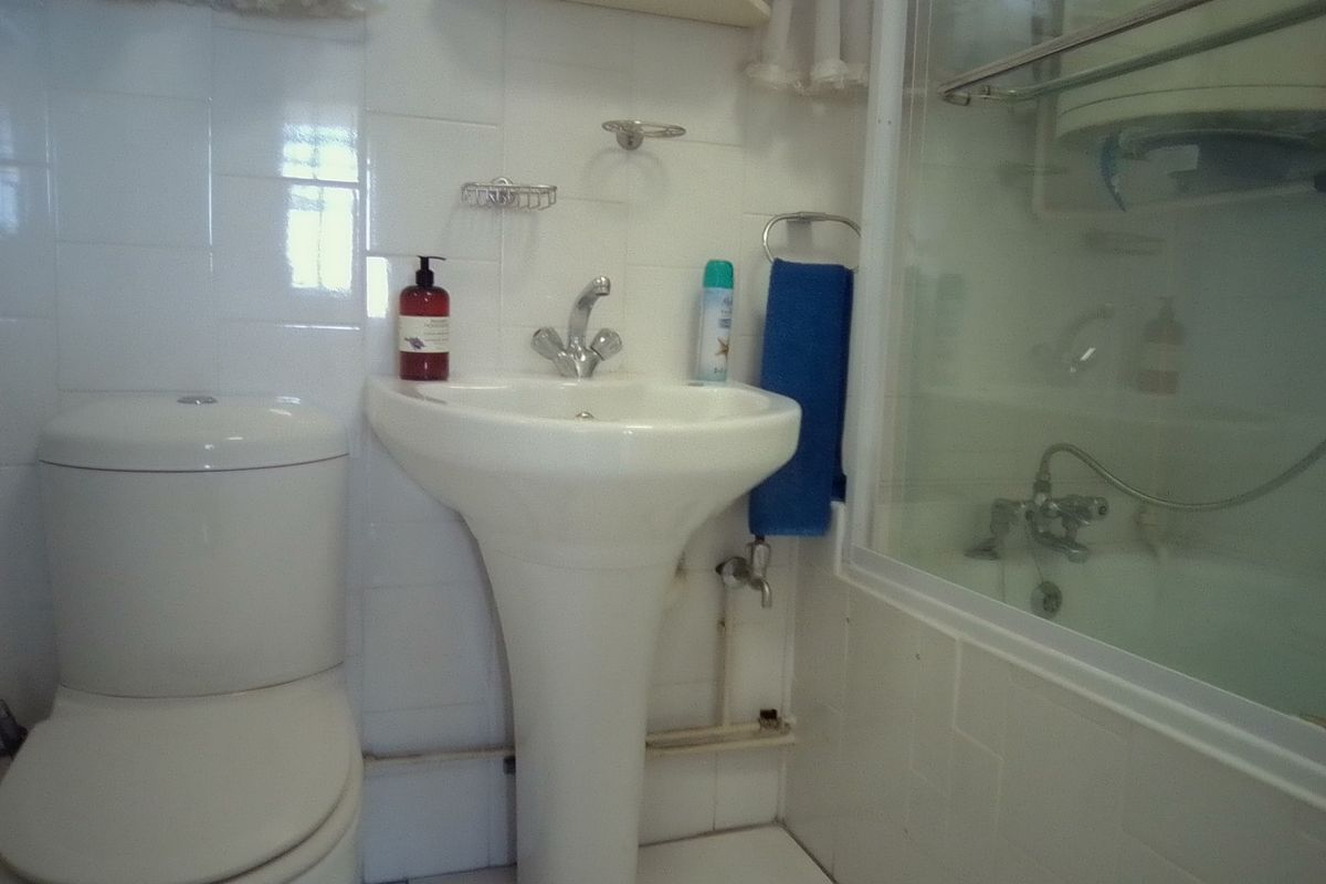 A compact bathroom featuring a pedestal basin, toilet, and a bathtub with a shower screen, finished with white wall and floor tiles.