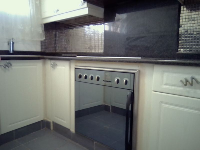 A functional kitchen featuring built-in oven, granite countertops, and mosaic tile backsplash with white cabinetry and tiled flooring.