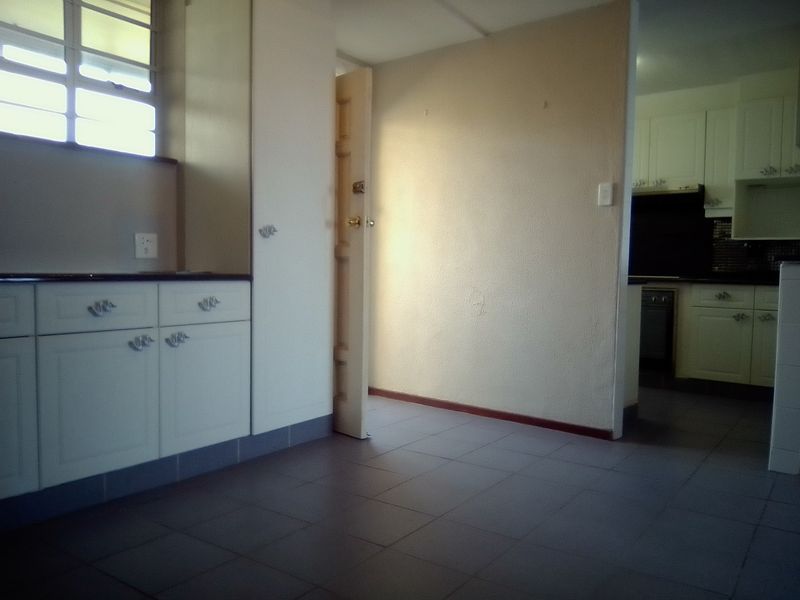 An empty kitchen area featuring tiled flooring, built-in cabinetry, and a view through to the adjacent cooking space.