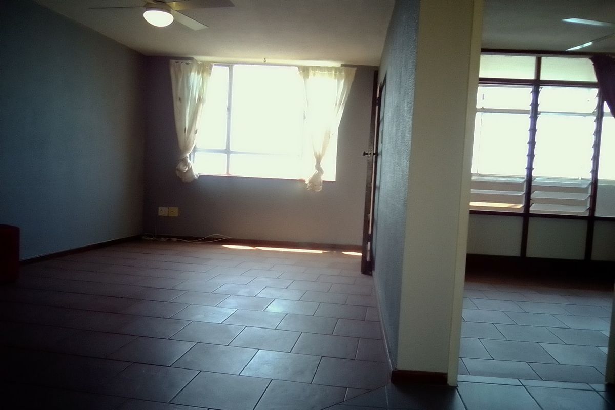 An empty living area featuring tiled flooring, a ceiling fan, and natural light from large windows.